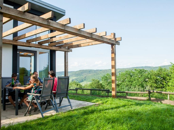Een gezin zit op het overdekte terras van hun vakantiewoning en geniet van het weidse uitzicht over de wijnvelden van de Moezel.