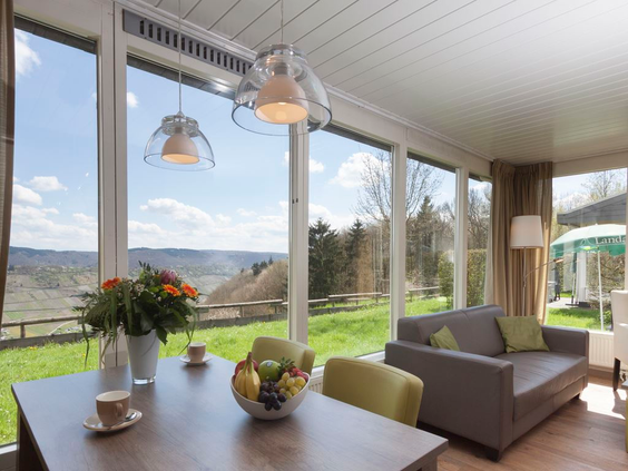 De sfeervolle en moderne woonkamer van een vakantiehuis op Landal Mont Royal, met grote ramen die uitkijken over het heuvelachtige landschap.