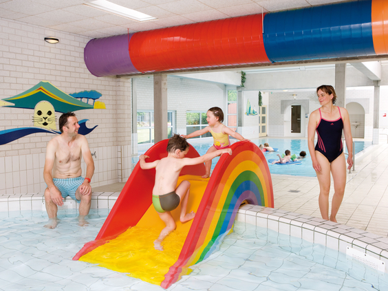 Kinderen spelen in het overdekte zwembad en glijden van een vrolijke regenboog kinderglijbaan bij Landal Natuurdorp Suyderoogh.
