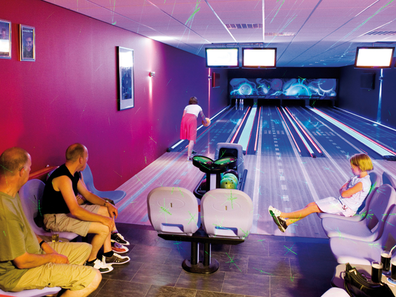Groep mensen aan het bowlen op een moderne bowlingbaan met sfeervolle, gekleurde verlichting bij Landal Natuurdorp Suyderoogh.