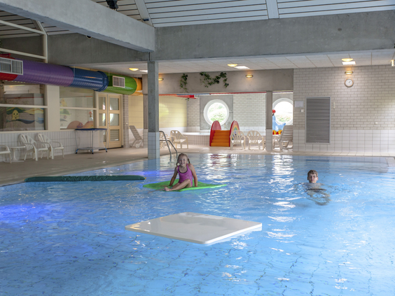 Kinderen spelen met een vlot en hebben plezier in het heldere water van het overdekte zwembad van Landal Natuurdorp Suyderoogh.