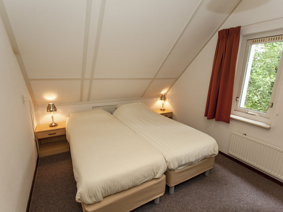 Nette slaapkamer met twee opgemaakte eenpersoonsbedden onder een schuin dak in een vakantiehuisje op Landal Natuurdorp Suyderoogh.