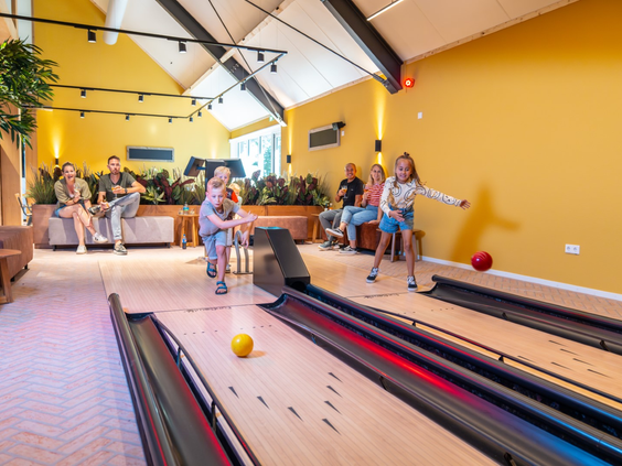 Kinderen en volwassenen gooien een bal op de bowlingbaan tijdens een potje bowlen op Landal Orveltermarke.