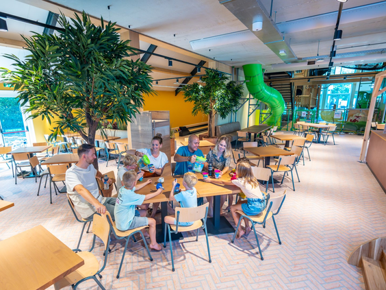 Gezinnen zitten aan tafels in het sfeervolle restaurant van Landal Orveltermarke, direct naast de indoorspeeltuin.