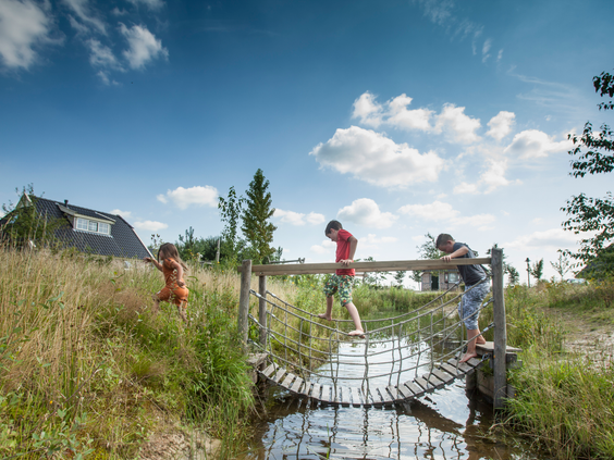 Kinderen steken voorzichtig een wiebelende touwbrug over het water over op het Avontureneiland van Landal Orveltermarke.