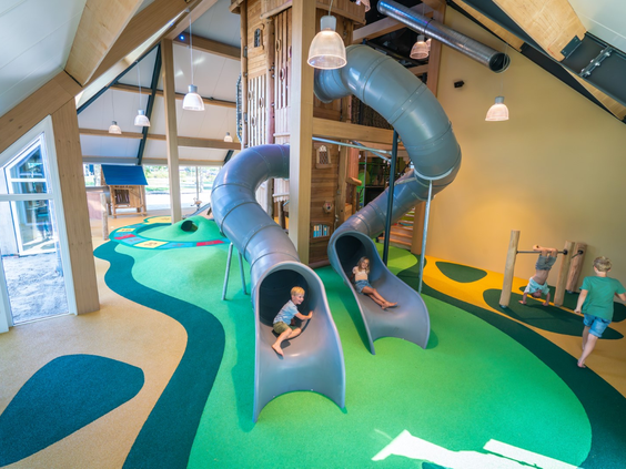 Kinderen glijden van de hoge, kronkelende tunnelglijbanen in het overdekte speelparadijs van Landal Orveltermarke.