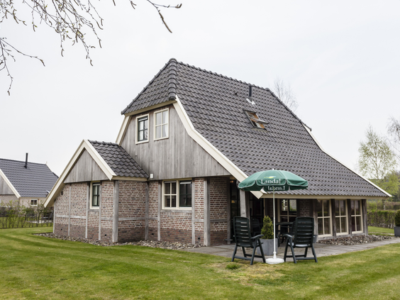 Achterkant van een ruime boerderijbungalow met een gemeubileerd terras en een groot grasveld op Landal Orveltermarke.
