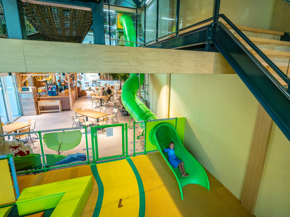 Kind glijdt van een lange groene glijbaan naar een lagere verdieping in het centrumgebouw van Landal Orveltermarke.