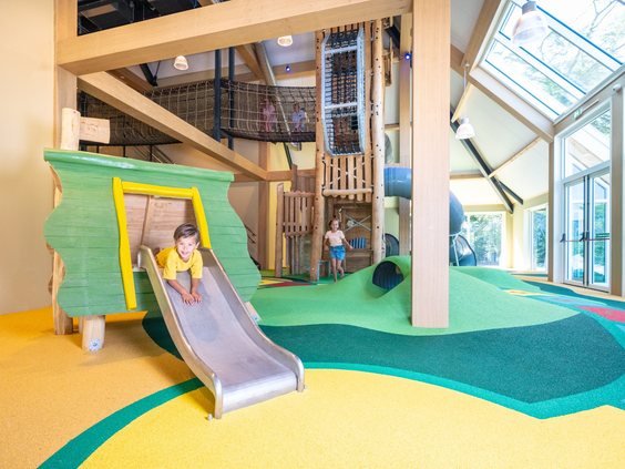 Klein kind op een brede glijbaan in de speciaal ingerichte peuterhoek van het indoor speelparadijs op Landal Orveltermarke.
