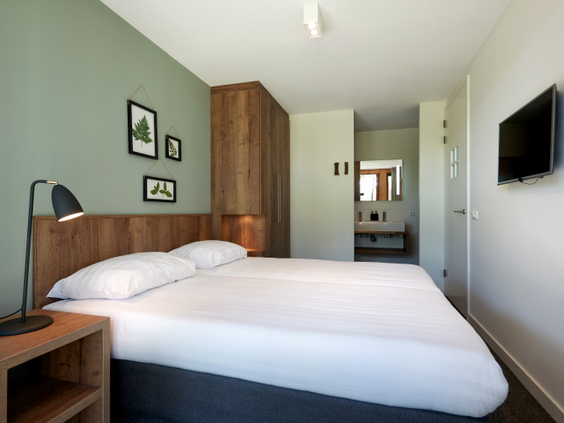 Stijlvolle slaapkamer met een comfortabel opgemaakt tweepersoonsbed en een eigen en-suite badkamer in een villa op Landal Puur Exloo.