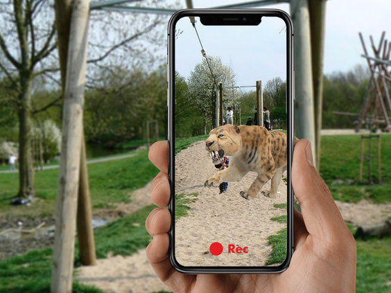 Een smartphone toont een sabeltandtijger via een augmented reality app, waardoor het lijkt alsof het prehistorische dier op het vakantiepark rondloopt.