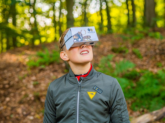 Een jongen met een virtual reality bril kijkt omhoog in het bos, klaar voor een digitaal avontuur in de omgeving van Landal Puur Exloo.