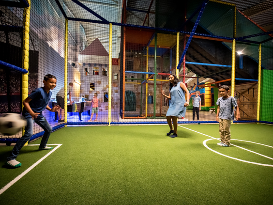 Een groep kinderen speelt voetbal op het indoor kunstgras sportveld, dat deel uitmaakt van de grote binnenspeeltuin op Landal Rabbit Hill.