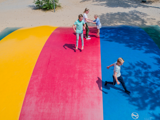 Een groep kinderen springt en rent vol plezier op de grote, kleurrijke airtrampoline, ofwel het luchtkussen, van Landal Rabbit Hill.
