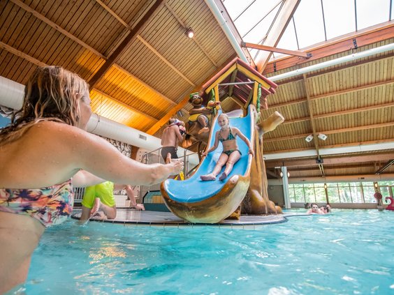 Een meisje glijdt lachend van de glijbaan in het overdekte zwembad en plonst in het water bij haar moeder op vakantiepark Landal Rabbit Hill.