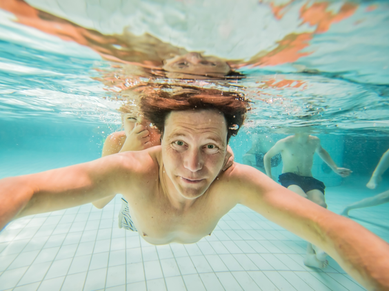 Een jongeman maakt een selfie terwijl hij onder water zwemt in het heldere blauwe water van het binnenzwembad op Landal Rabbit Hill.