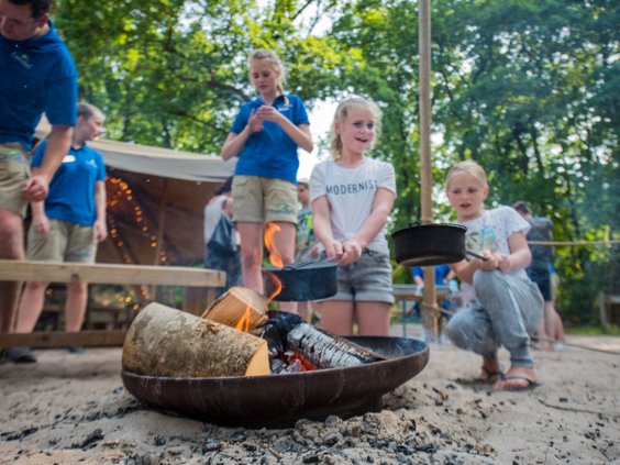 Een groep kinderen staat rond een vuurschaal in het bos en bakt zelf broodjes boven het vuur tijdens een activiteit op Landal Rabbit Hill.