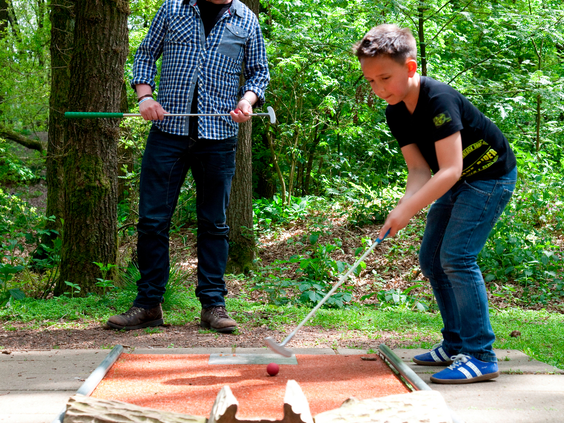 Een jongen concentreert zich op het putten van de bal tijdens een potje midgetgolf op de bosrijke baan van Landal Rabbit Hill.