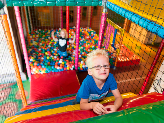 Twee jongens spelen in de kleurrijke binnenspeeltuin van Landal Rabbit Hill, met een van hen die van de glijbaan de ballenbak in glijdt.