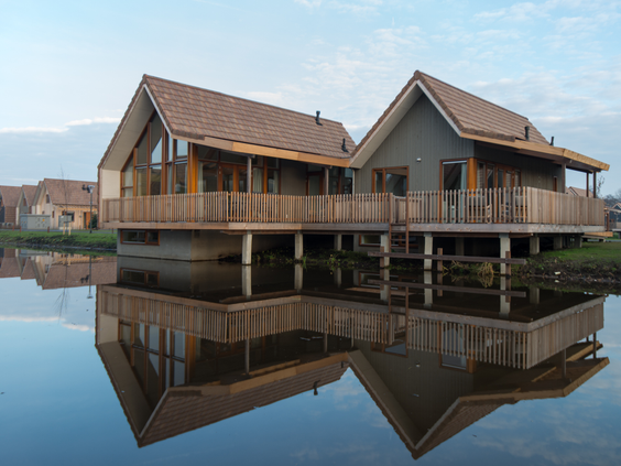 Een luxe, vrijstaande waterwoning op palen met een houten veranda, die prachtig reflecteert in het kalme water van de Reeuwijkse Plassen bij Landal.