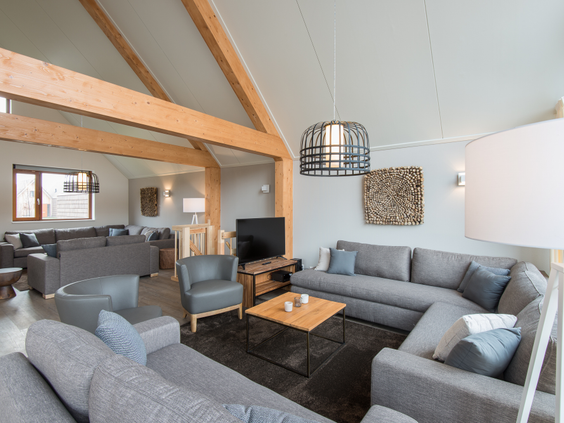 De zeer ruime woonkamer van een groepsbungalow op Landal Reeuwijkse Plassen, met meerdere grote, comfortabele hoekbanken onder een hoog plafond met houten balken.