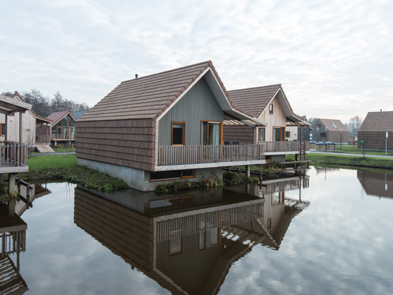 Twee moderne, houten waterwoningen met veranda's die direct aan het kabbelende water van de Reeuwijkse Plassen liggen.