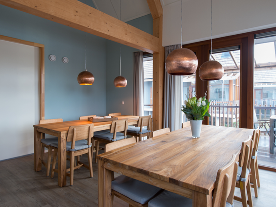 De ruime eetkamer van een groepsbungalow op Landal Reeuwijkse Plassen, ingericht met lange houten eettafels en moderne koperen lampen.