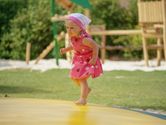 Een vrolijk meisje in een roze jurk springt op de grote gele airtrampoline in de speeltuin van Landal Salztal Paradies.