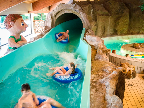 Kinderen komen met opblaasbanden uit een glijbaantunnel en plonzen in het zwembad van Landal Salztal Paradies.