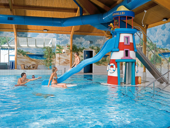 Kinderen spelen in het overdekte zwembad van Landal Sluftervallei op Texel, met een blauwe waterglijbaan die uitkomt bij een vrolijke vuurtoren.