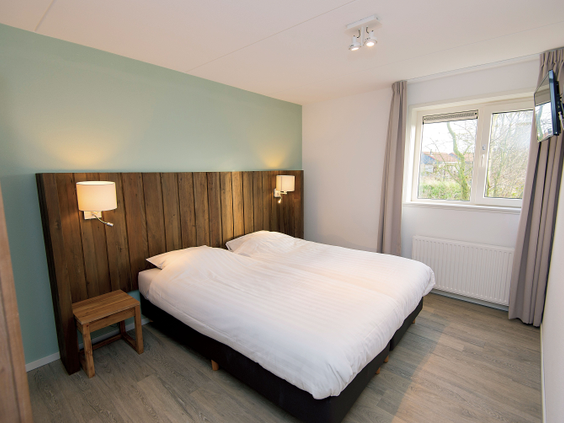 Een netjes opgemaakt tweepersoonsbed met een wit dekbed en een houten hoofdeinde in een moderne slaapkamer van een bungalow op Landal Sluftervallei.