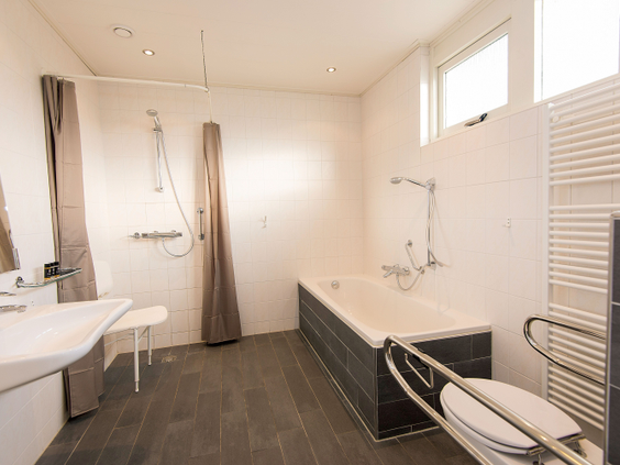 Een ruime, aangepaste badkamer voor mindervaliden met een douche, een bad met beugels en een verlaagde wastafel in een speciale bungalow op Landal Sluftervallei.