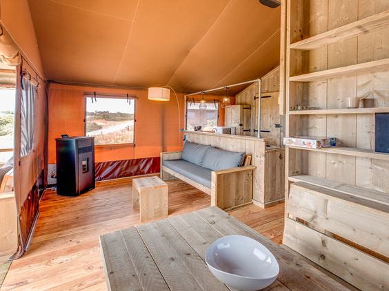 De houten binnenkant van een luxe safaritent op Landal Sluftervallei, met een eettafel, zithoek en uitzicht op de Texelse duinen.