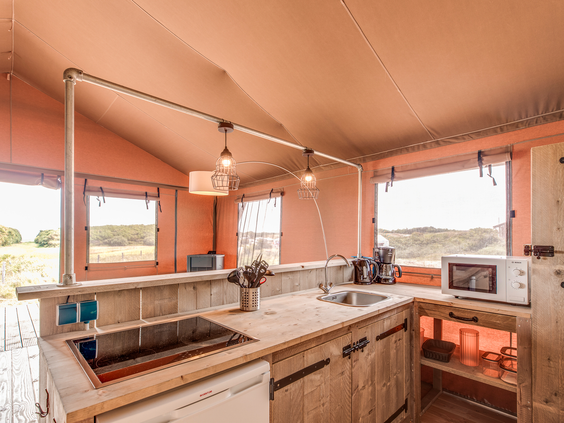Een volledig ingerichte houten keuken met een fornuis, wasbak, magnetron en koffiezetapparaat in een safaritent op Landal Sluftervallei.