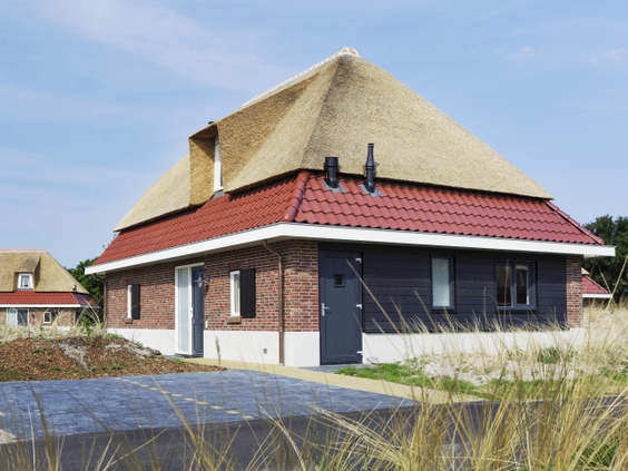 Een luxe, vrijstaande vakantiewoning met een rieten dak en een terras, gelegen in het duingras van vakantiepark Landal Sluftervallei op Texel.