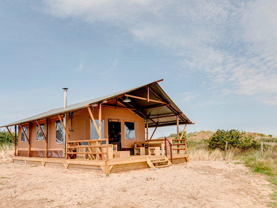Een stoere en luxe safaritent met een houten veranda, gelegen op een zandheuvel in de duinen van Landal Sluftervallei op Texel.