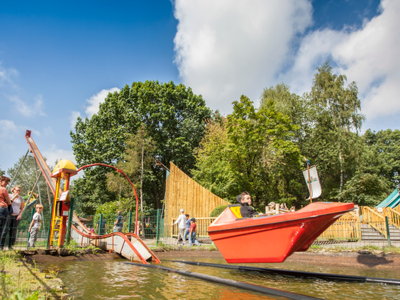 Kinderen spelen in een avontuurlijke waterspeeltuin met een rode speelboot en een kabelbaan op Landal Sneekermeer.
