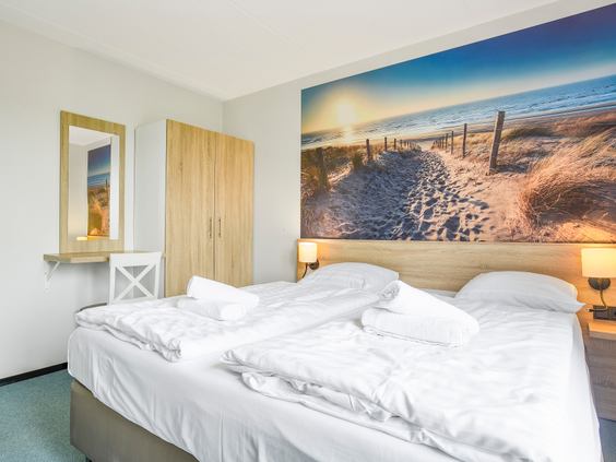 Comfortabele slaapkamer met een tweepersoonsbed en sfeervol fotobehang van een duinlandschap in een huisje op Landal Sneekermeer.
