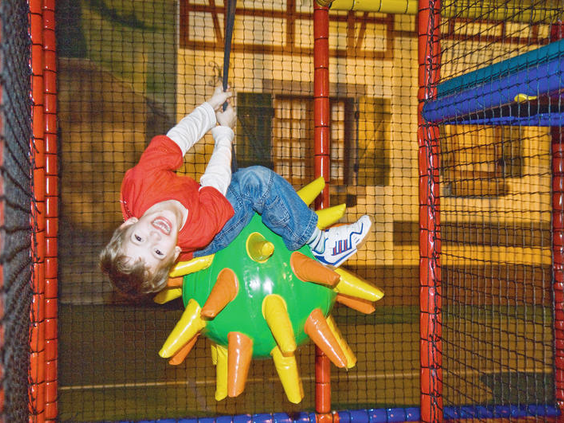 Een kind hangt lachend ondersteboven aan een draaiend speeltoestel in het grote indoor speelparadijs van Landal Sonnenberg.