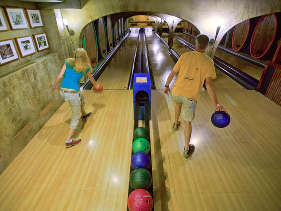 Een familie is aan het bowlen op de sfeervolle bowlingbaan, die is ingericht als een gezellige wijnkelder, op Landal Sonnenberg.