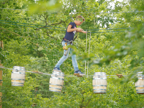 Een stoere jongen balanceert over hangende tonnen op het avontuurlijke hoogteparcours in het klimbos van Landal Sonnenberg.