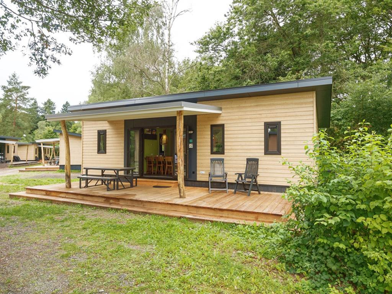 De buitenkant van een moderne houten chalet met een ruim terras en tuinmeubilair op vakantiepark Landal Sonnenberg.