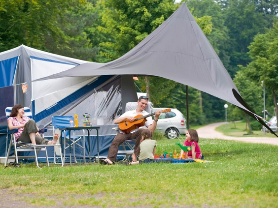 Een gezin geniet van het campingleven op een ruime kampeerplaats bij Landal Sonnenberg, waarbij de vader gitaar speelt voor zijn kinderen.
