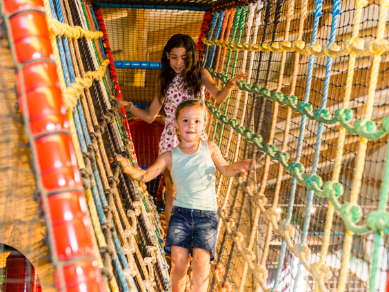 Kinderen klimmen over een wiebelige touwbrug in het grote indoor speelparadijs van vakantiepark Landal Sonnenberg.
