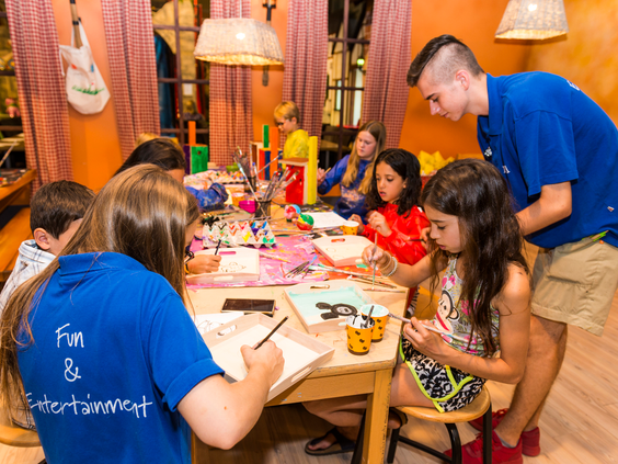 Kinderen zijn gezellig aan het knutselen aan een lange tafel, begeleid door het Fun & Entertainment team in de Bollo Club van Landal Sonnenberg.