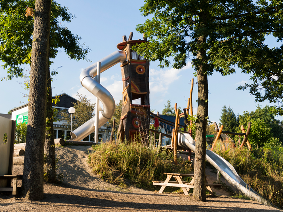 Een grote buitenspeeltuin met een hoge, kronkelende glijbaantoren tussen de bomen op vakantiepark Landal Sonnenberg.