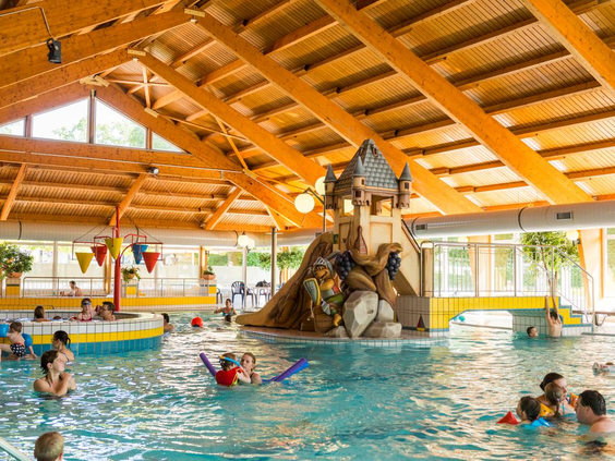 Het overdekte zwembad van Landal Sonnenberg met een leuk speelkasteel en glijbaan in het water voor kinderen.