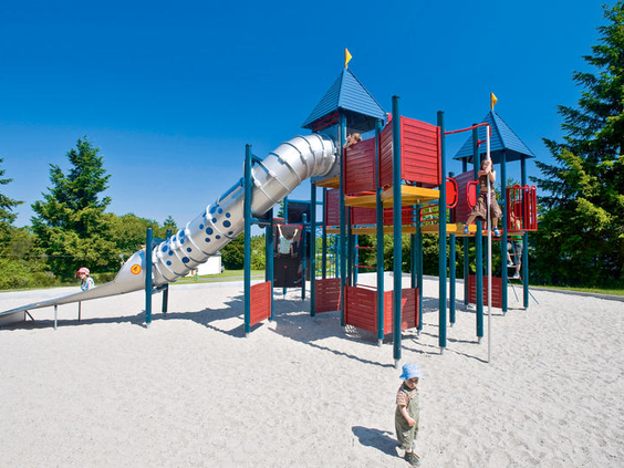 Kinderen spelen in een kleurrijke buitenspeeltuin met een grote glijbaan en klimrek in ee