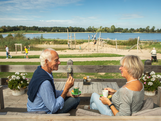 Opa en oma genieten van een drankje op het terras met uitzicht op de recreatieplas en de speeltuin van Landal Stroombroek.