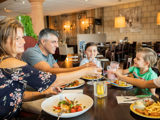 Gezin met kinderen geniet samen van een diner en proost met drankjes in het sfeervolle restaurant van Landal Stroombroek.
